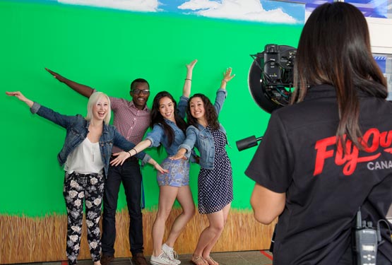 Four people pose with "airplane arms" for a photo in front of a green screen