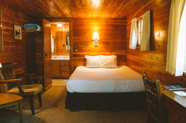 The inside of a rustic wooden cabin, with a warm glowing lamp above a bed