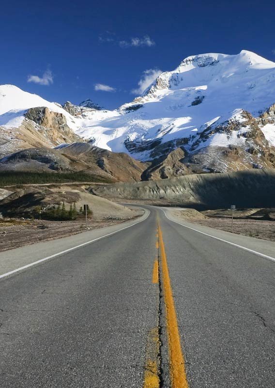 A road stretches towards ice-covered mountains.
