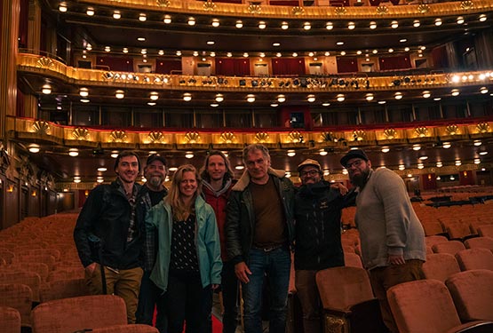 A group of people smile at the camera as they stand inside a large theatre with rows of seats.