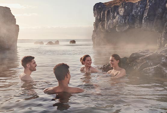 Four friends sit together in a spa pool between rock formations.