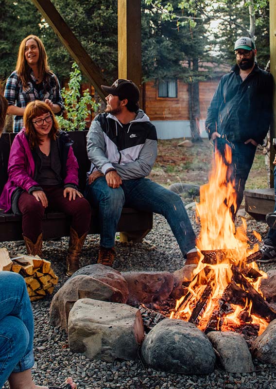 A group of people sit around a bonfire laughing and smiling
