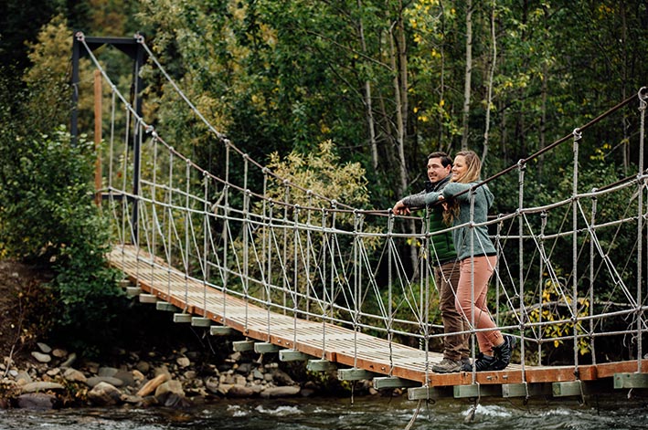 Two hikers stand on a small suspension foot bridge.