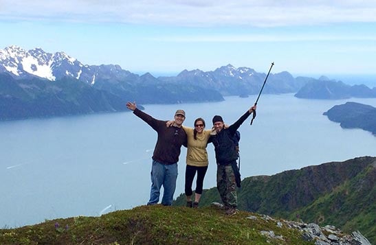 Three people stand at a mountain above the sea.