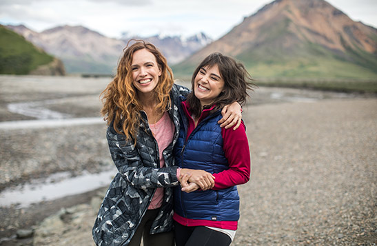 Two women hugging and smiling with mountains and river in the background