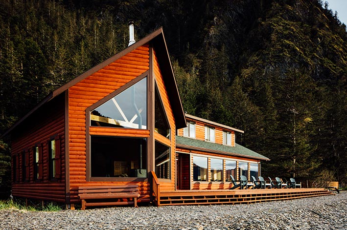 A rustic wooden lodge between a rocky beach and forested mountainside