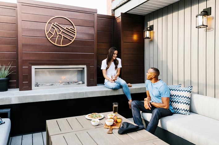 Two people sit on a rooftop patio enjoying snacks and drinks,