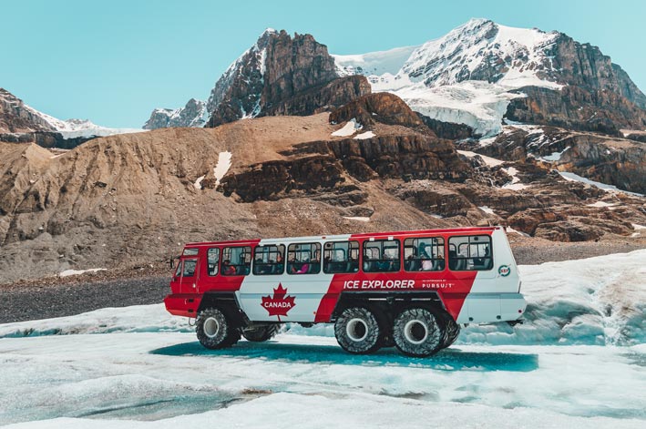 A red and white Ice Explorer vehicle moved on an ice road below a rocky mountainside