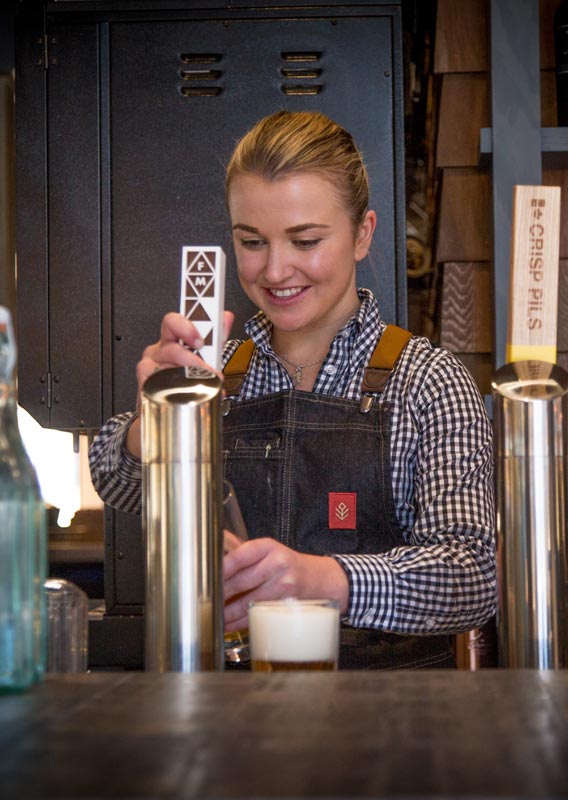 A bartender pours a pint of beer from a draught tap.