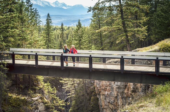 Two people stand on a bridge over a deep canyon