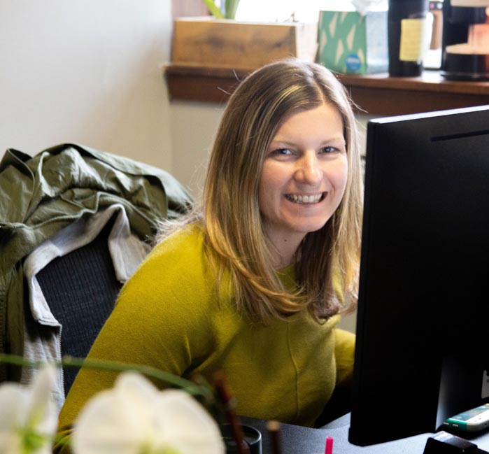 A woman smiles while working at a computer desk.