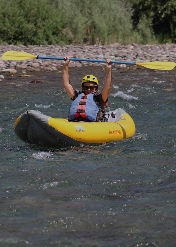 A man in a yellow single raft with his paddle held above his head in the water.