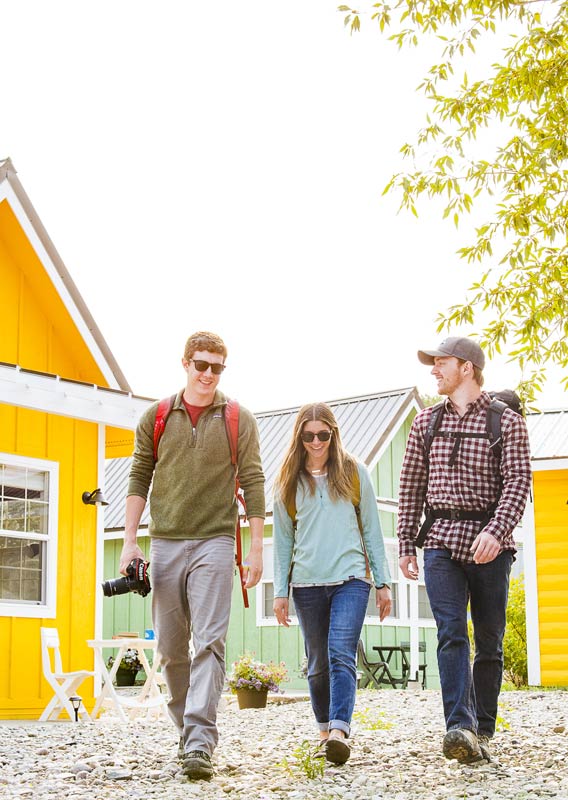 Three people ready for a hike walk between colorful tiny homes
