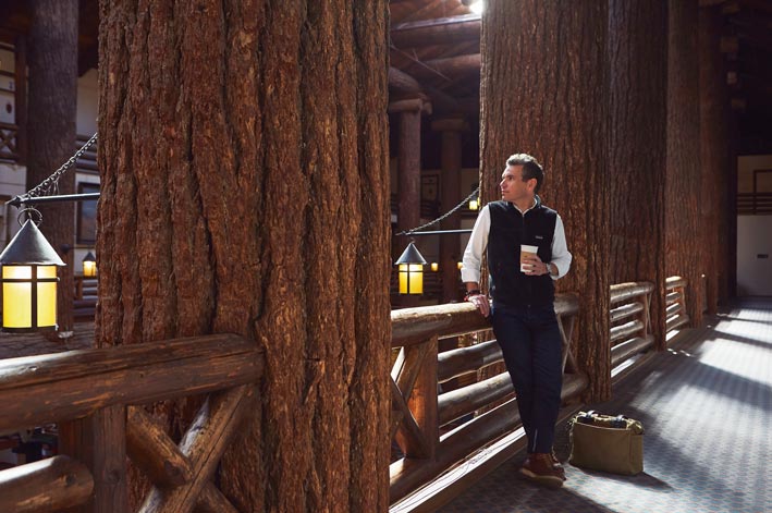 A man stands between large douglas fir tree trunk beams.