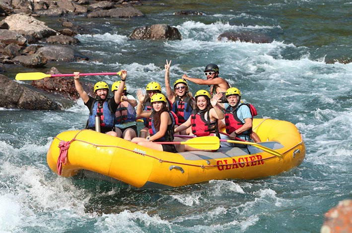 A group of rafters smile and wave to the camera while on a raft in the water