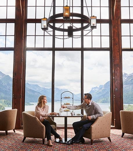 Two people sitting at a dining table in a restaurant with tall windows and a view of mountains.