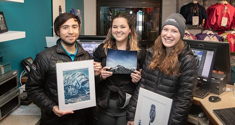 Three people hold nature photography prints.