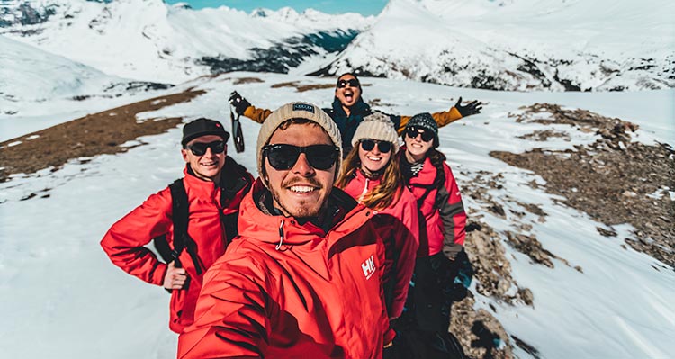A group of five people smile for a selfie on a snowy mountain ridge.