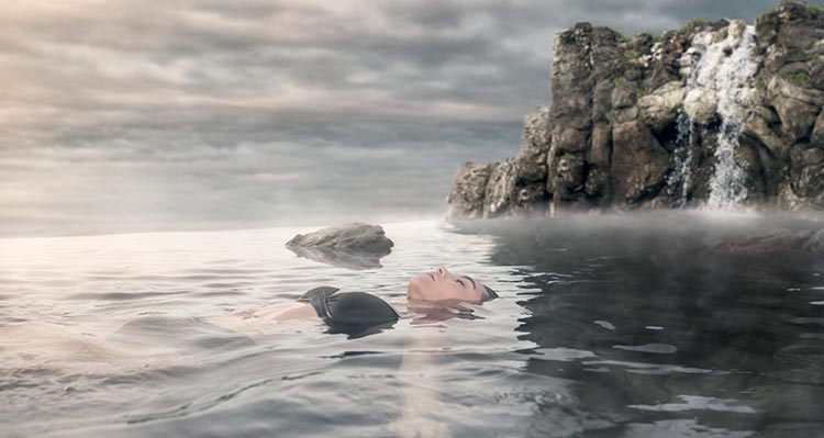A person floats in a pool by a rocky shoreside.