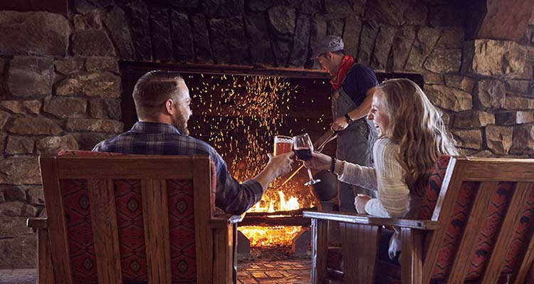 A couple enjoy a beer and wine while sitting across from the fireplace