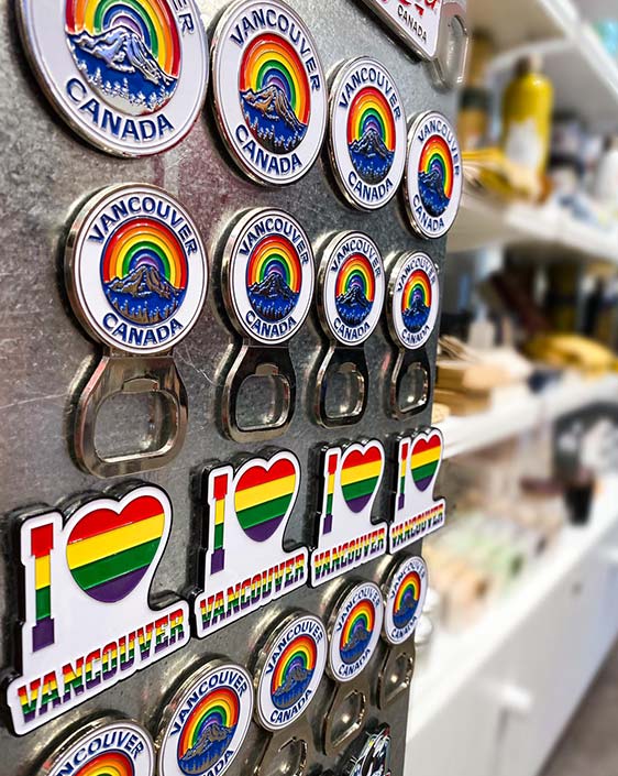 A wall of magnets in a gift shop that show Vancouver Canada with a rainbow around it.
